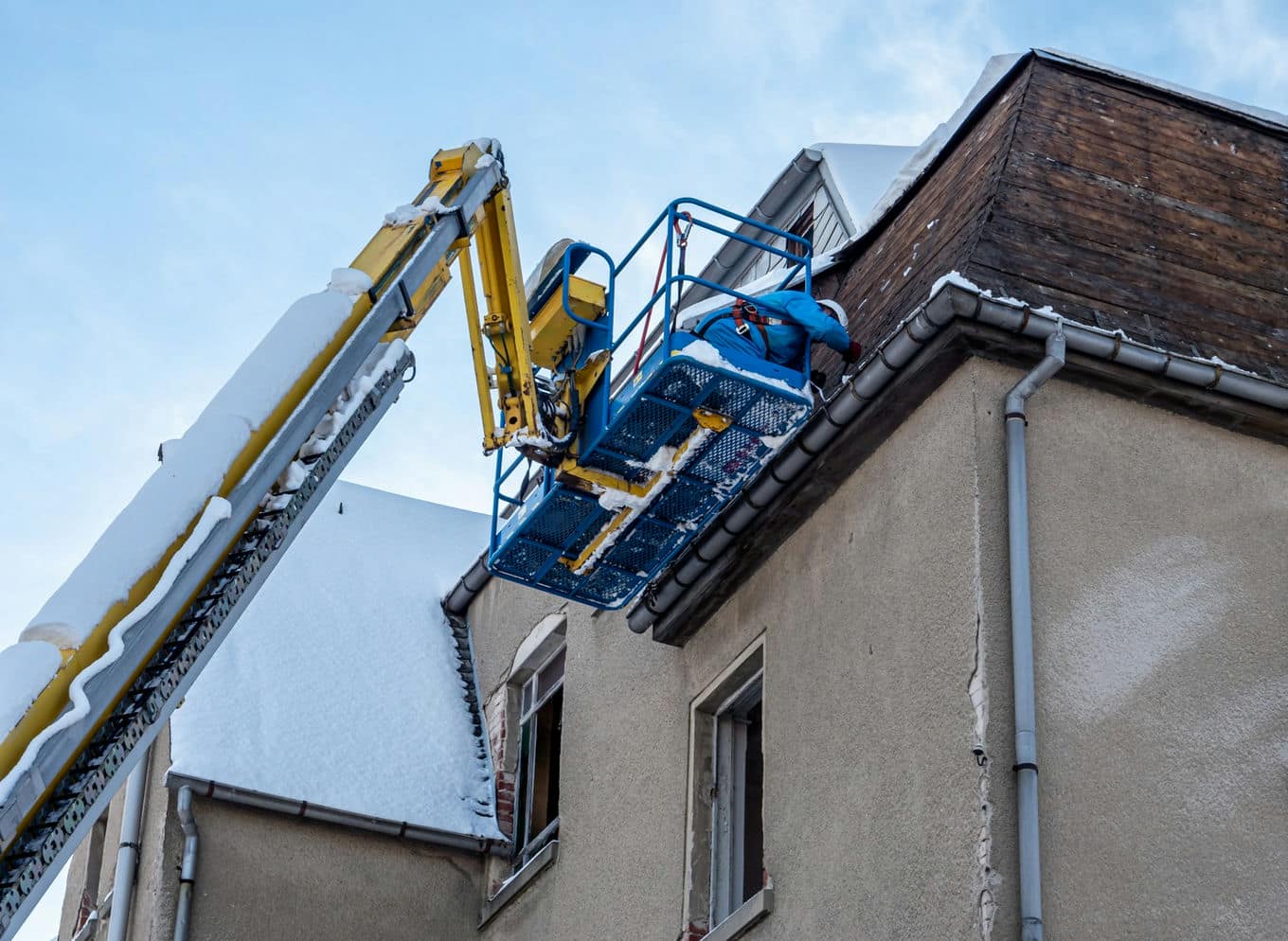 mężczyzna na podnośniku odśnieża dach